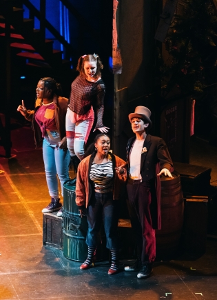 Four actors in RENT singing together on elevated platforms