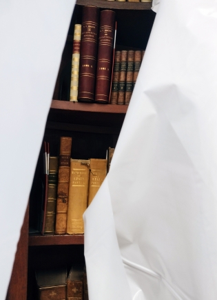 Books on a shelf partially covered with a plastic sheet