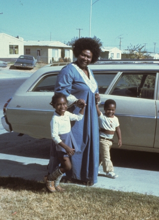 Ruby Duncan holds the hands of two children on a sunny driveway.
