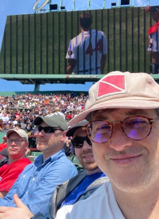 Selfie of four men at a Red Sox baseball game on a sunny day.