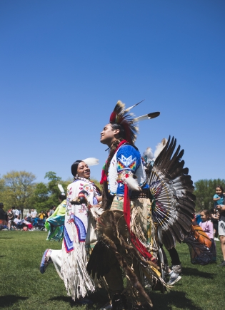 People dancing at Powwow, wearing feathers and a head dress